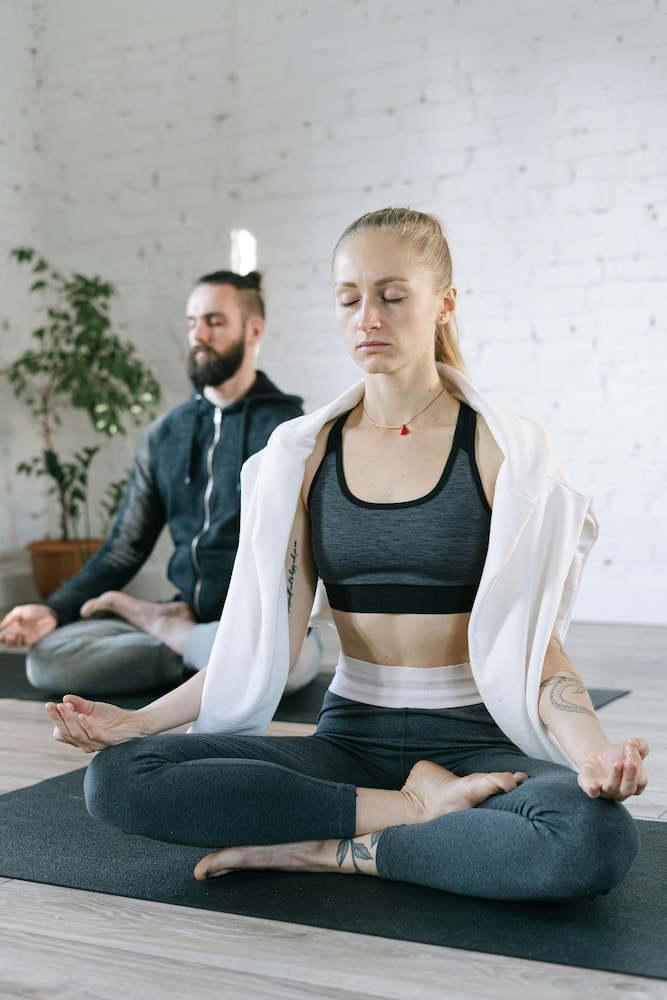 woman and man meditating on yoga mats in a bright minimalist indoor setting